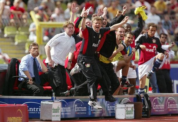 Trainer Klaus Augenthaler (li.) bleibt völlig stoisch während die komplette Bank jubelnd aufspringt, vorn v. li.: Torwarttrainer Harald Schumacher und Co-Trainer Peter Hermann (alle Leverkusen) Fußball 1. BL Herren Saison 2002 2003, Nürnberg - Bayer 04 Leverkusen 0:1, gefasst, Ruhepol, Kontrast Gruppe Nürnberg Ruhe Freude, Begeisterung