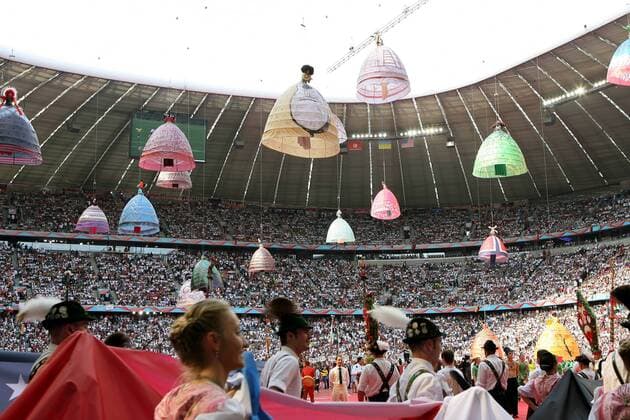 Eröffnungsfeier zur FIFA Weltmeisterschaft 2006: Frauen in überdimensionalen Röcken schweben vom Dach des Münchener WM Stadions zu Boden, wo gerade eine bayrische Trachtengruppe einmarschiert Fußball WM Herren Weltmeisterschaft 2006, Eröffnung, Feier, Zeremonie, Totale World Cup Stadium, Worldcup München