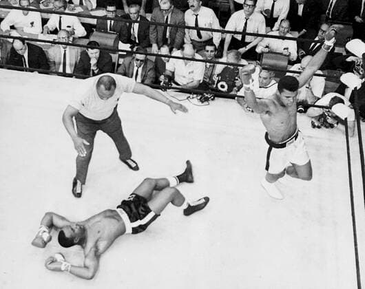 Overhead view showing Sonny Liston on the canvas as Cassius Clay celebrates his victory in the first round of their title fight in Lewiston, Maine. 25th May 1965  UnitedArchives00925585