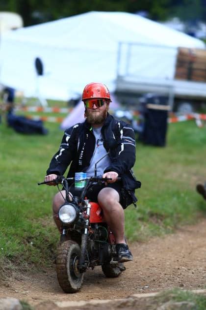 An enthusiastic fan explores the grounds of the ADAC RAVENOL 24h Nürburgring on a red motorcycle on Thursday, May 14, 2026 Wearing a red helmet and black motorcycle jacket, he rides over the muddy edge of the track, while barrier beacons and the race track infrastructure are visible in the background Fan on motorcycle at the Nürburgring - 24h Race 2026 Copyright: xspeedshotx