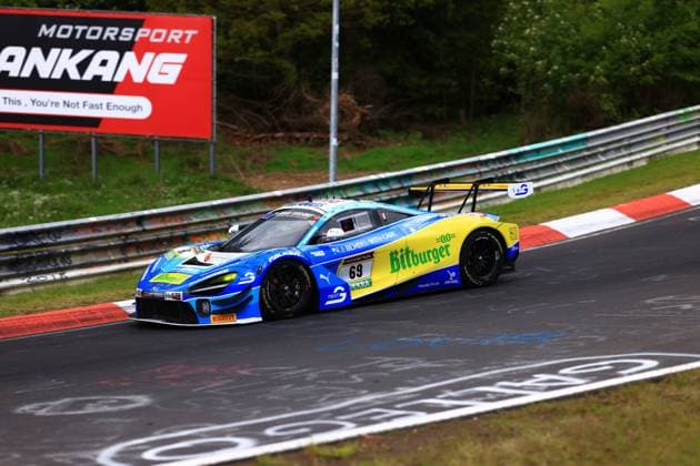 The McLaren GT3 with starting number 69 from Doerr Motorsport - driven by Ben Dörr, Marvin Kirchhöfer, Timo Glock and Timo Scheider - takes a corner on the Nordschleife of the Nürburgring The car Ben Doerr Marvin Kirchhöfer Timo Glock Timo Scheider Doerr Motorsport is painted in the team colors blue and yellow with prominent Bitburger sponsoring and shows yellow rims and a striking rear wing In the background you can see a billboard of Motorsport Ankang McLaren 69 from Doerr Motorsport on the Nordschleife Copyright: xspeedshotx