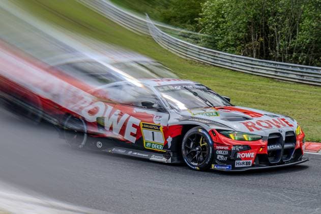 Dynamic panning shot of Augusto Farfus Jordan Pepper Kelvin van der Linde Raffaele Marciello ROWE RACING by ROWE RACING on the Nürburgring Nordschleife The BMW M4 GT3 with the starting number 1 and the characteristic red, black and white ROWE design is captured sharply in the picture, while the background and an overtaking car on the left are impressively blurred by the panning movement of the camera The sponsors RAVENOL, DEKRA, Michelin and H R as well as the BMW M Motorsport logo are clearly visible The car is on the asphalt track of the Nordschleife with a green embankment and crash barriers in the background ROWE RACING BMW M4 GT3 1 with panning effect on the Nordschleife Copyright: xspeedshotx