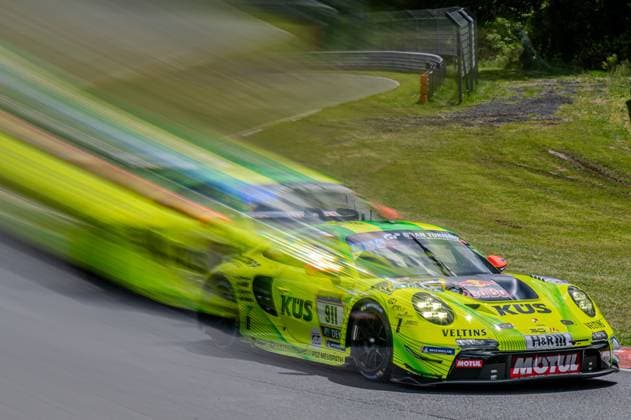 The Ayhancan Güven Kevin Estre Thomas Preining Manthey from Manthey in characteristic neon yellow green with KÜS, Veltins, Red Bull and Motul sponsorship chases with impressive speed through the Nordschleife at the 24h Nürburgring The panning shot creates a strong motion blur effect in the background and emphasizes the high speed of the Porsche 911 GT3 R The track layout with catch fence and boundary posts can be seen in the background Manthey Porsche 911 GT3 R at full speed on the Nordschleife Copyright: xspeedshotx