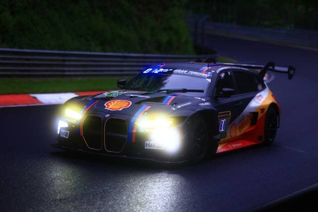 The BMW M4 GT3 with starting number 81 from BMW M Motorsport drives through a corner of the Nordschleife at the Nürburgring at dusk The car wears a characteristic dark livery with the classic BMW Motorsport stripes in blue, red and orange as well as striking Shell and H R sponsor logos The switched-on headlights shine brightly in the gathering darkness, The wet asphalt reflects the light The Connor de Phillippi Jens Klingmann Neil Verhagen Ugo de Wilde BMW M Motorsport is seen from the front in a dynamic drive, surrounded by the typical red kerbs and crash barriers of the Nordschleife BMW M4 GT3 81 from BMW M Motorsport at dusk on the Nordschleife Copyright: xspeedshotx
