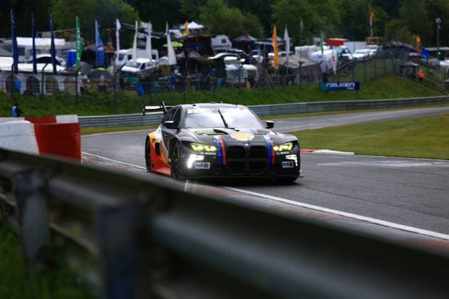 A matt black BMW M4 GT3 Luca Engstler Mirko Bortolotti Patric Niederhauser Red Bull Team ABT drives through a bend on the Nürburgring The car wears the characteristic Red Bull livery with the distinctive bull logo on the flank and the BMW Motorsport colors blue violet red as vertical stripes on the front Sponsors such as Bosch, H R and Shell are visible on the bodywork Flags, team tents and the paddock of the 24-hour race can be seen in the background BMW M4 GT3 on the Nürburgring circuit Copyright: xMichaelxGelhardtx