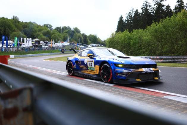 The Christopher Mies Dennis Olsen Emil Christian Gjerdrum Finn Wiebelhaus Frederic Vervisch HRT Ford Racing Ford Mustang GT3 with the starting number 64 from HRT Ford Racing drives through a corner on the Nürburgring The vehicle wears a striking blue and gold livery with RAVENOL and DEKRA sponsorship as well as the Ford Racing and Haupt Racing Team lettering The characteristic crash barriers, green vegetation and the spectator infrastructure of the Nürburgring can be seen in the background Ford Mustang GT3 64 from HRT Ford Racing on the Nürburgring Copyright: xMichaelxGelhardtx