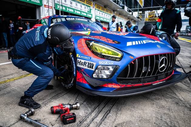 In the pit lane of the Nürburgring, a Mercedes AMG Team Verstappen Racing mechanic works on the Daniel Juncadella Jules Gounon Lucas Auer Max Verstappen Mercedes AMG Team Verstappen Racing The mechanic changes a tire on the blue and red Mercedes AMG GT3, while a pneumatic wrench lies ready on the ground The car bears the sponsors H R, Sparco and Michelin as well as the Gran Turismo lettering on the hood Other team members and the pit wall with DEKRA advertising banners are visible in the background Mercedes AMG GT3 3 from Verstappen Racing changing tires in the pits Copyright: xMichaelxGelhardtx