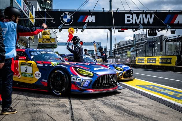 The Mercedes AMG GT3 with starting number 3 of the Mercedes AMG Team Verstappen Racing is parked in the pit lane of the Nürburgring A crew member in helmet and racing suit has just left the vehicle, while other team members accompany the pit stop A second golden vehicle can be seen in the pit lane in the background The sponsors RAVENOL, Falken, H R and Red Bull are clearly visible on the striking blue and red paintwork The BMW M banner can be seen above the pit lane Mercedes AMG GT3 3 from Verstappen Racing in the pit lane Copyright: xMichaelxGelhardtx