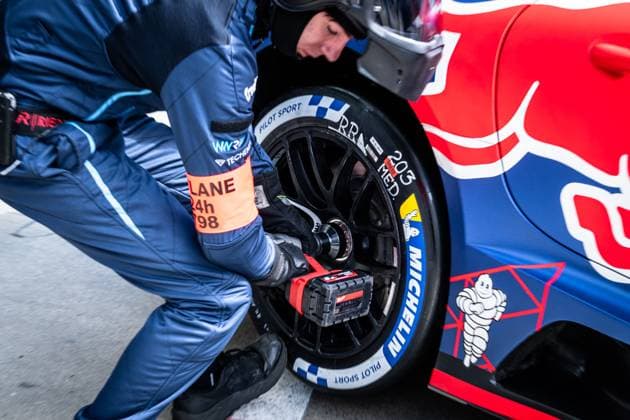 A mechanic uses a battery-powered impact wrench to change a tire on a vehicle with Red Bull livery The pit lane marking 24h P98 can be read on the sleeve tape The Michelin Pilot Sport tire is pulled while the blue and red vehicle is in the pits Changing tires in the pits at the 24h Nürburgring Copyright: xMichaelxGelhardtx