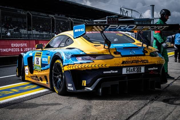The Mercedes AMG GT3 with starting number 26 from PROsport Racing is parked in the pit lane at the Nürburgring The car Adam Christodoulou Christopher Lulham Marek Böckmann Mikaël Grenier PROsport Racing presents an eye-catching yellow and blue Pixel Design Livery with sponsors such as RAVENOL, Bilstein, H R and Goodyear In the background, track marshals and the pit wall with spectator stands can be seen Mercedes AMG GT3 26 from PROsport Racing in the pit lane Copyright: xMichaelxGelhardtx