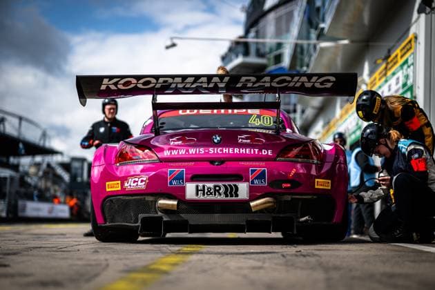 The magenta-colored BMW Z4 GT3 with starting number 40 stands in the pit lane at the Nürburgring Mechanics from the W I S Racing Team powered by Koopman Racing work on the car, while the striking rear wing with the Koopman Racing lettering catches the eye Sponsors such as H R, Pirelli, JCC Racing and W I S safety are prominently displayed on the bodywork The car Frank Nikolaus Michael Funke Peter Posavac W I S Racing Team powered by Koopman Racing being prepared for the next stint BMW Z4 GT3 40 by W I S Racing Team in the pits at the Nürburgring Copyright: xMichaelxGelhardtx