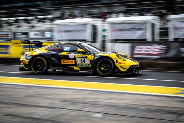 The Porsche 911 GT3 with the starting number 54 of the Dinamic GT team drives through the pit lane at the Nürburgring at high speed The black and yellow car Bastian Buss Michael Christensen Michael Klitgaard Christensen Dinamic GT bears the sponsors Pirelli, RAVENOL, DEKRA and HRX prominently on the bodywork The characteristic black and yellow paintwork and the large rear wing of the Porsche GT3 are clearly recognizable Porsche 911 GT3 54 from Dinamic GT in the pit lane at the Nürburgring Copyright: xMichaelxGelhardtx