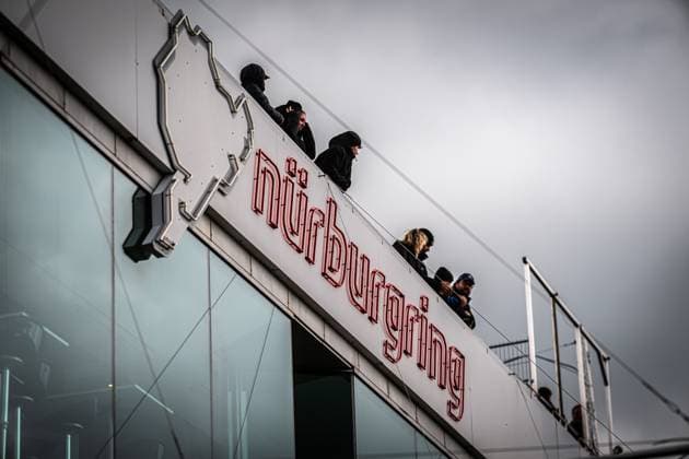 Several people stand on a viewing platform above the striking Nürburgring lettering in red neon lettering The iconic logo with the track outline is clearly recognizable The overcast sky gives the atmosphere a typical Eifel character at the 24h Nürburgring 2026 Spectators watch the action at the Nürburgring building Copyright: xMichaelxGelhardtx
