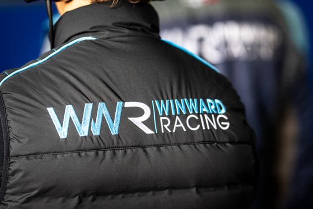 A Winward Racing team member wears a black quilted jacket with the distinctive WNR logo and Winward Racing lettering in the Nürburgring paddock Another team member in the same team clothing can be seen in the background Winward Racing team member at the 24h Nürburgring 2026 Copyright: xMichaelxGelhardtx