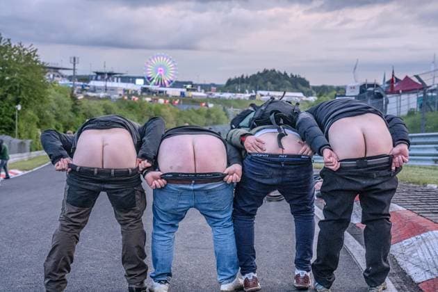 Four fans present a classic mooning moment directly on the asphalt of the race track at the Nürburgring The illuminated Ferris wheel of the paddock and the infrastructure of the event site can be seen in the background The exuberant mood reflects the unique atmosphere of the 24-hour race weekend Fans show off their butts on the track at the Nürburgring Copyright: xMichaelxSchäferx