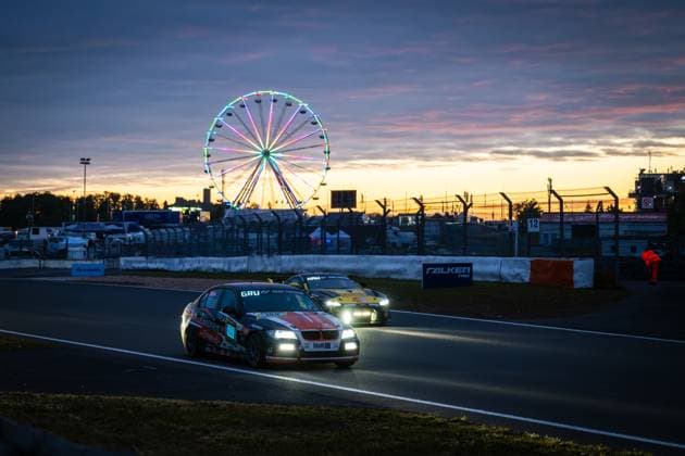The BMW 3 Series of EiFelkind Racing Christopher Gruber Henning Hausmeier Markus Fischer Michael Fischer Oliver Frisse Pistorius by EiFelkind Racing rolls around the Nürburgring Grand Prix circuit at dusk The car with starting number 100 wears the striking orange, black and white livery with GRU Gran Turismo and H R sponsorship Behind it follows another vehicle in low beam In the background, the illuminated Ferris wheel of the paddock shines colorfully against a dramatic sunset sky in orange and purple The track signage with Falken Tyres and the Hyundai banner are recognizable BMW 100 from EiFelkind Racing at sunset at the Nürburgring Copyright: xMichaelxGelhardtx