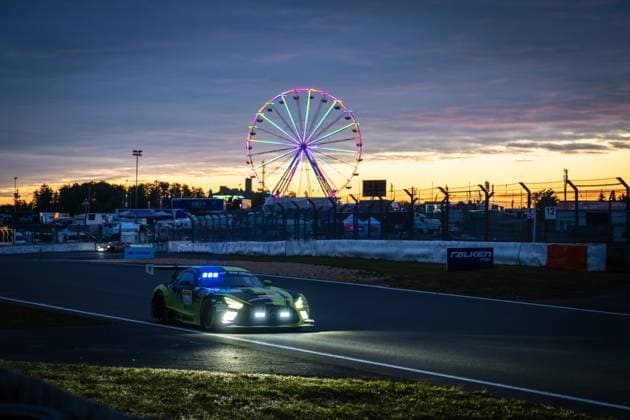 A black neon yellow Mercedes AMG GT3 drives through a curve at the Nürburgring at dusk The switched-on headlights and the blue roof lights shine brightly in the falling darkness In the background, a colorfully illuminated Ferris wheel shines in orange and blue tones against a dramatic sunset sky A Falken Tyres banner is visible on the track boundary The starting number is not clearly legible in the backlight and due to the motion blur Mercedes AMG GT3 in the sunset at the Nürburgring with Ferris wheel Copyright: xMichaelxGelhardtx