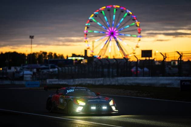 The Mercedes AMG GT3 racing car from Goroyan RT by Car Collection drives over the Nürburgring at dusk The switched-on headlights shine intensely, while in the background a colorfully illuminated Ferris wheel shines against an orange sunset sky The vehicle wears the Red Bull livery with eye-catching artwork The atmospheric atmosphere underlines the character of the ADAC RAVENOL 24h Nürburgring Mercedes AMG GT3 4 by Goroyan RT at sunset at the Nürburgring Copyright: xMichaelxGelhardtx