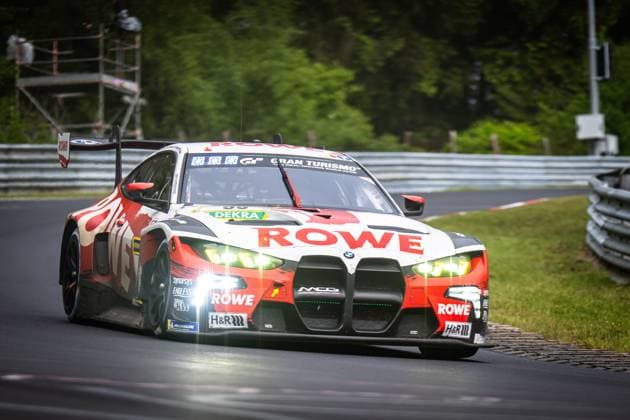 The BMW M4 GT3 Dan Harper Dries Vanthoor Max Hesse Sheldon van der Linde ROWE RACING from ROWE RACING takes a corner on the Nordschleife of the Nürburgring The car in the characteristic red and white ROWE livery has the headlights switched on and displays a dynamic driving stance Sponsors such as DEKRA, H R and Michelin are clearly visible on the bodywork BMW M4 GT3 99 from ROWE RACING on the Nordschleife Copyright: xMichaelxGelhardtx