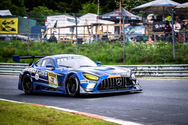 The Mercedes AMG GT3 Andreas Gülden Tim Sandtler Yuichi Nakayama Toyo Tires with Ring Racing from Toyo Tires with Ring Racing drives through a bend on the Nordschleife of the Nürburgring The blue and gold vehicle with the distinctive Toyo Tires and RAVENOL logos has visible accident damage on the front end - body parts are secured with makeshift tape The yellow headlights are illuminated, spectators and tent structures can be seen in the background Mercedes AMG GT3 32 from Toyo Tires with Ring Racing on the Nordschleife Copyright: xMichaelxGelhardtx