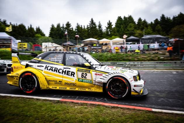 Luca Ludwig Markus Winkelhock Sebastian Asch HWA Engineering Speed from HWA Engineering Speed drives at high speed through a corner on the Nordschleife at the Nürburgring The striking yellow and white vehicle bears prominent sponsor logos such as Kärcher, RAVENOL, SONAX and bluechem GROUP The wet asphalt reflects the overcast weather of the Eifel, with spectators and hospitality tents visible in the background Mercedes AMG 62 from HWA Engineering Speed on the Nordschleife Copyright: xMichaelxGelhardtx