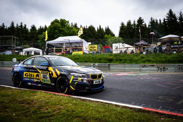 The BMW M235i Racing 665 LG Bamberg from GITI TIRE MOTORSPORT BY WS RACING drives through a bend on the Nordschleife at the Nürburgring The vehicle wears the striking black and yellow Giti livery with eye-catching camouflage patterns Clearly visible sponsors are Giti Competition Tires, RAVENOL and DEKRA Spectators, tents and the characteristic green vegetation of the Eifel can be seen in the background BMW M235i Racing 665 from GITI TIRE MOTORSPORT BY WS RACING on the Nordschleife Copyright: xMichaelxGelhardtx