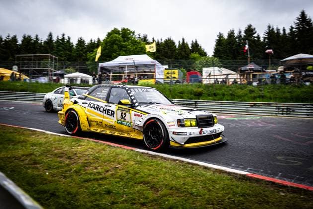 The Mercedes Benz 190E Evolution from HWA Engineering Speed with starting number 62 negotiates a bend on the Nordschleife of the Nürburgring The striking yellow and white vehicle with KÄRCHER and RAVENOL sponsorship presents itself in a classic racing car design with a modern aerodynamics package Another vehicle and the paddock with spectators and tents can be seen in the background The race takes place in cloudy weather The placeholder Luca Ludwig Markus Winkelhock Sebastian Asch HWA Engineering Speed marks this vehicle Mercedes Benz 190E 62 from HWA Engineering Speed on the Nordschleife Copyright: xMichaelxGelhardtx