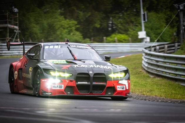 The BMW M4 GT3 Jens Klingmann Ugo de Wilde Schubert Motorsport by Schubert Motorsport takes a corner on the Nordschleife of the Nürburgring The car wears a striking black and red livery with prominent Yokohama and ADVAN sponsors as well as H R suspension technology The headlights shine brightly as the car glides over the asphalt with an active rear wing BMW M4 GT3 81 by Schubert Motorsport on the Nordschleife Copyright: xMichaelxGelhardtx