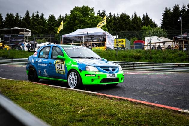 The Dacia Logan Robert Neumann Alexander Becker Christian Geilfus Gregor Starck Oliver Kriese Ollis Garage Racing from Ollis Garage Racing drives through a curve on the Nürburgring The vehicle is painted in an eye-catching blue and green color scheme and bears sponsors such as RAVENOL, DEKRA, Falken, Goodyear, junited AUTOGLAS, H R and Bleker Autoteile Spectators, yellow flags and a white tent can be seen in the background Dacia Logan 300 from Ollis Garage Racing on the Nürburgring Copyright: xMichaelxGelhardtx