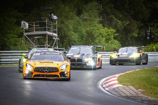 The orange Mercedes AMG GT3 of Mercedes AMG Team RAVENOL Fabian Schiller Luca Stolz Maro Engel Maxime Martin Mercedes AMG Team RAVENOL leads a group of cars through a bend on the Nordschleife at the Nürburgring With its headlights switched on and the distinctive RAVENOL sponsorship, the car takes the apex of the bend. A BMW M4 GT3 and another car follow in the background - both with their lights switched on A green car can also be seen on the left of the picture A camera bridge with photographers is set up in the background Mercedes AMG GT3 80 from Mercedes AMG Team RAVENOL on the Nordschleife Copyright: xMichaelxGelhardtx