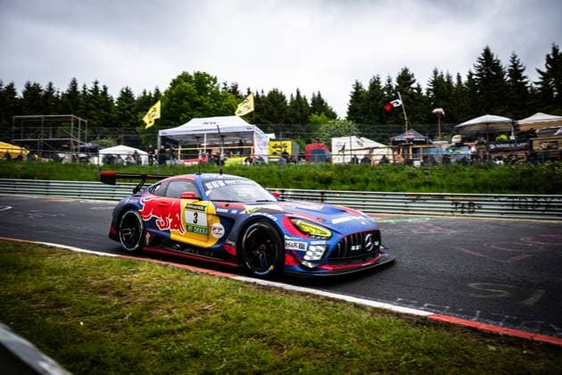 The Mercedes AMG GT3 Daniel Juncadella Jules Gounon Lucas Auer Max Verstappen Mercedes AMG Team Verstappen Racing from Mercedes AMG Team Verstappen Racing drives through a fast corner on the Nürburgring Nordschleife The car wears the characteristic Red Bull livery in blue, red and yellow with RAVENOL and DEKRA sponsorship Spectators, tents and yellow flags of the 24h race can be seen in the background Mercedes AMG GT3 3 from Verstappen Racing on the Nordschleife Copyright: xMichaelxGelhardtx