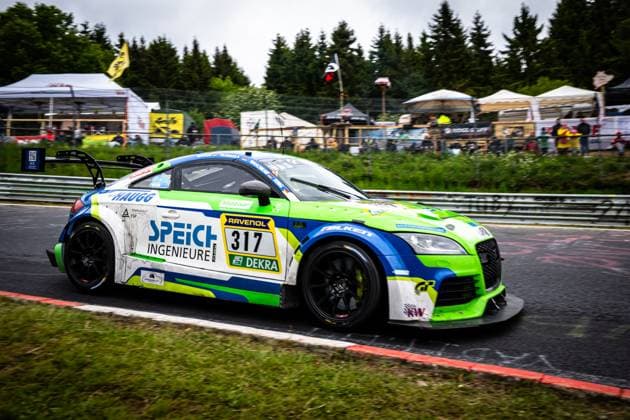 The Audi TT RS from 2R Racing passes a section of the Nordschleife at the Nürburgring with starting number 317 The vehicle Roland Waschkau Dirk Vleugels Thorsten Jung Wolfgang Haugg 2R Racing wears a striking green, blue and white livery with the sponsors Speich Ingenieure GmbH, RAVENOL and Falken Spectators and hospitality tents from the team camps can be seen in the background as the vehicle drives through the bend with motion blur Audi TT 317 from 2R Racing on the Nordschleife Copyright: xMichaelxGelhardtx