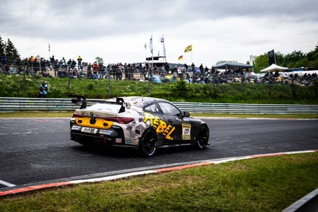The BMW M4 GT4 Alexandru Vasilescu David Ogburn Malcolm Harrison Mark Smith Sergiu Nicolae AV Racing by BLACK FALCON from AV Racing by BLACK FALCON drives through a corner on the Nürburgring The vehicle has a striking camouflage design in gray and black with striking yellow accents and the REBEL lettering Numerous sponsors such as LIQUI MOLY, Fanatec and H R are visible on the bodywork In the background, numerous spectators follow the racing action at the ADAC RAVENOL 24h Nürburgring BMW M4 GT4 177 from AV Racing by BLACK FALCON at the Nürburgring Copyright: xMichaelxGelhardtx