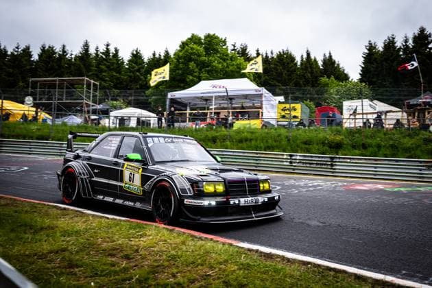 The striking black Mercedes 190E with starting number 61 from HWA Engineering Speed takes a bend on the Nordschleife of the Nürburgring The vehicle presents itself with a wide aero package, yellow headlights and eye-catching red tire sidewalls Sponsors such as RAVENOL, DEKRA and H R are clearly visible In the background, spectators watch the race under an overcast sky Bruno Spengler Christian Gebhardt Evald Holstad Peter Ludwig HWA Engineering Speed Mercedes 190E 61 from HWA Engineering Speed on the Nordschleife Copyright: xMichaelxGelhardtx