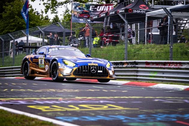 The Mercedes AMG GT3 80 from Mercedes AMG Team RAVENOL drives through a corner on the Nordschleife of the Nürburgring with its headlights switched on The vehicle wears the characteristic blue and gold livery with RAVENOL and H R sponsorship and is painted in the typical Gran Turismo design In the background, numerous spectators watch the race behind the catch fence Fabian Schiller Luca Stolz Maro Engel Maxime Martin Mercedes AMG Team RAVENOL Mercedes AMG GT3 80 from RAVENOL on the Nordschleife Copyright: xMichaelxGelhardtx