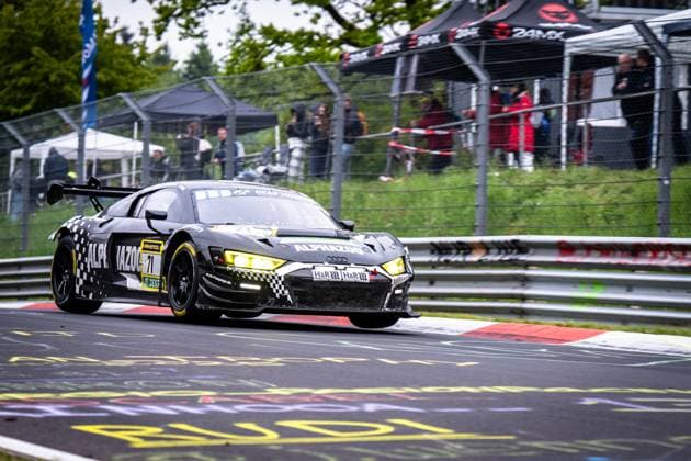 The Audi R8 LMS GT3 Björn Großmann Christer Jöns Otto Blank Pierre Kaffer JUTA Racing from JUTA Racing takes a corner on the Nordschleife of the Nürburgring The black and white checkered car with yellow headlights bears the sponsors ALPHAZOO, RAVENOL and H R In the background, spectators behind the safety fence follow the racing action The characteristic red curbs of the Nordschleife are clearly visible Audi R8 LMS GT3 71 from JUTA Racing on the Nordschleife Copyright: xMichaelxGelhardtx
