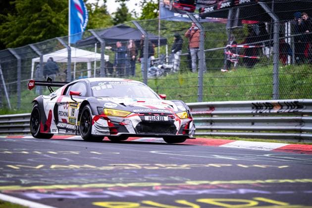 The Audi R8 LMS GT3 Christian Kohlhaas Duncan Huismann Jan Jaap van Roon Rudy van Buren Max Kruse Racing from Max Kruse Racing drives through a corner on the Nordschleife of the Nürburgring The car bears the starting number 19 and features a striking white, red and gray camouflage design with sponsors such as MASCOT WORKWEAR, RAVENOL and H R In the background, spectators follow the race behind the catch fence Audi R8 LMS GT3 19 from Max Kruse Racing on the Nordschleife Copyright: xMichaelxGelhardtx