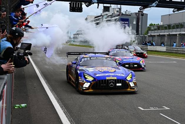 The Mercedes AMG GT3 80 from Mercedes AMG Team RAVENOL drives through the pit lane of the Nürburgring with the smoke generator activated for the show drive The blue and gold vehicle with RAVENOL branding is cheered by spectators and media representatives, while several other GT3 racing cars follow Mercedes AMG GT3 80 from Mercedes AMG Team RAVENOL in the pit lane Copyright: xMichaelxGelhardtx