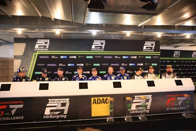 Nine drivers sit at a press conference at the Nürburgring The line-up shows drivers from Mercedes AMG Team RAVENOL 80 and Red Bull Team ABT 84 with the recognized drivers Christian Krognes, Fabian Schiller, Luca Stolz, Maro Engel, Maxime Martin and Mirko Bortolotti In the background are sponsoring bands with RAVENOL, ADAC, Monster Energy, H R and other partners visible Drivers briefing at the ADAC RAVENOL 24h Nürburgring with Mercedes AMG and Red Bull teams Copyright: xspeedshotx