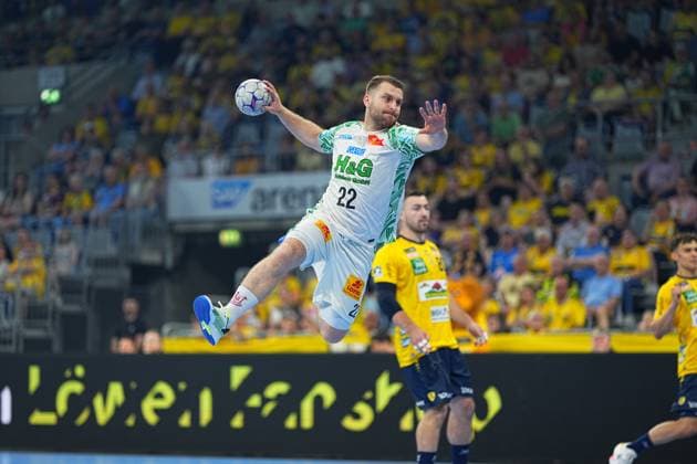 Magnus Saugstrup 23 SC Magdeburg jumps to shoot with the ball in his hand, while Jannik Kohlbacher 80 Rhein Neckar Löwen can be seen in the background The packed SAP Arena forms the backdrop for the DAIKIN HBL duel Magnus Saugstrup 23 SC Magdeburg taking a jump shot in the SAP Arena Copyright: xspeedshotx