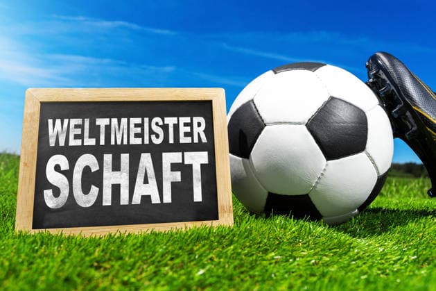 FOTOMONTAGE, Symbolfoto zur Fußball-Weltmeisterschaft 2026: Fußball, rote und gelbe Schiedsrichterkarten sowie eine Pfeife liegen auf grünem Spielfeldrasen neben einer Tafel mit dem Schriftzug Weltmeisterschaft.