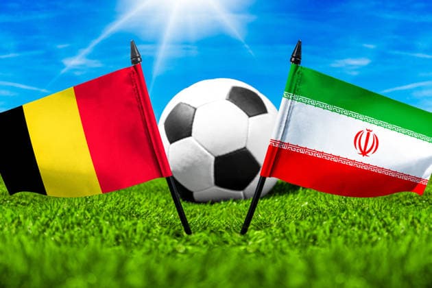 FOTOMONTAGE, Fußball-Weltmeisterschaft 2026: Nationalflaggen von Belgien und Iran mit Fußball auf Rasen. Symbolbild zum WM-Gruppenspiel am 21 Juni bei der FIFA Fussball-Weltmeisterschaft 2026