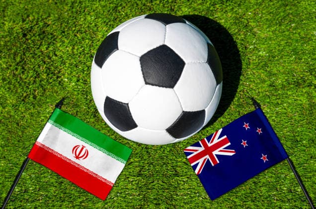 FOTOMONTAGE, Fußball-Weltmeisterschaft 2026: Nationalflaggen von Iran und Neuseeland mit Fußball auf Rasen. Symbolbild zum WM-Gruppenspiel am 16 Juni bei der FIFA Fussball-Weltmeisterschaft 2026