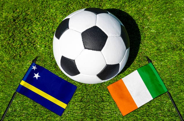 FOTOMONTAGE, Fußball-Weltmeisterschaft 2026: Nationalflaggen von Curacao und Elfenbeinküste mit Fußball auf Rasen. Symbolbild zum WM-Gruppenspiel am 25 Juni bei der FIFA Fussball-Weltmeisterschaft 2026