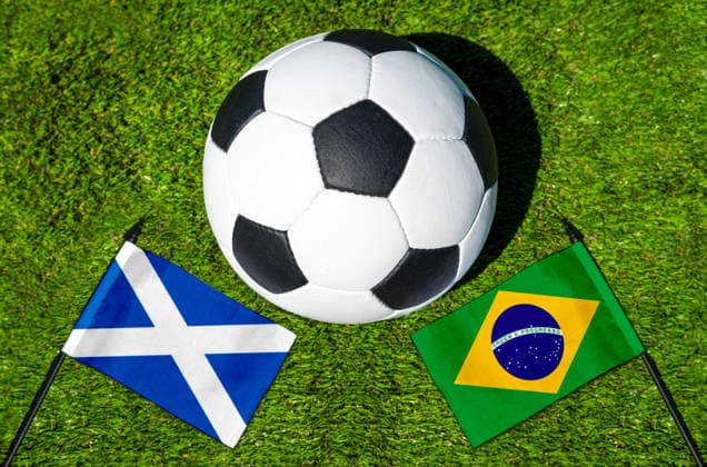 FOTOMONTAGE, Fußball-Weltmeisterschaft 2026: Nationalflaggen von Schottland und Brasilien mit Fußball auf Rasen. Symbolbild zum WM-Gruppenspiel am 25 Juni bei der FIFA Fussball-Weltmeisterschaft 2026