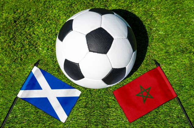 FOTOMONTAGE, Fußball-Weltmeisterschaft 2026: Nationalflaggen von Schottland und Marokko mit Fußball auf Rasen. Symbolbild zum WM-Gruppenspiel am 20 Juni bei der FIFA Fussball-Weltmeisterschaft 2026