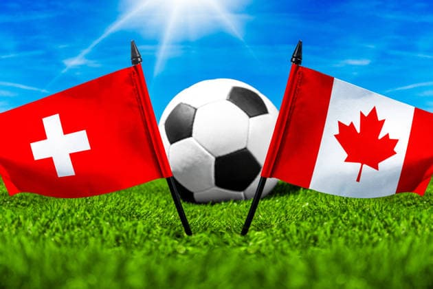 FOTOMONTAGE, Fußball-Weltmeisterschaft 2026: Nationalflaggen von Schweiz und Kanada mit Fußball auf Rasen. Symbolbild zum WM-Gruppenspiel am 24 Juni bei der FIFA Fussball-Weltmeisterschaft 2026