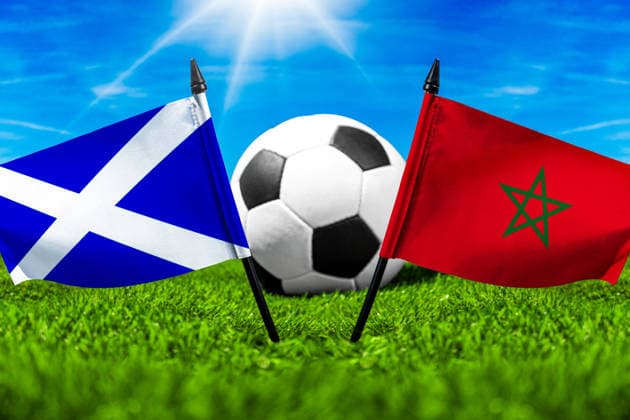 FOTOMONTAGE, Fußball-Weltmeisterschaft 2026: Nationalflaggen von Schottland und Marokko mit Fußball auf Rasen. Symbolbild zum WM-Gruppenspiel am 20 Juni bei der FIFA Fussball-Weltmeisterschaft 2026