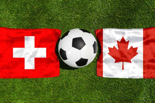 FOTOMONTAGE, Fußball-Weltmeisterschaft 2026: Nationalflaggen von Schweiz und Kanada mit Fußball auf Rasen. Symbolbild zum WM-Gruppenspiel am 24 Juni bei der FIFA Fussball-Weltmeisterschaft 2026