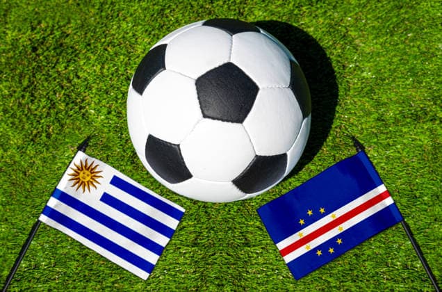 FOTOMONTAGE, Fußball-Weltmeisterschaft 2026: Nationalflaggen von Uruguay und Kap Verde mit Fußball auf Rasen. Symbolbild zum WM-Gruppenspiel am 22 Juni bei der FIFA Fussball-Weltmeisterschaft 2026
